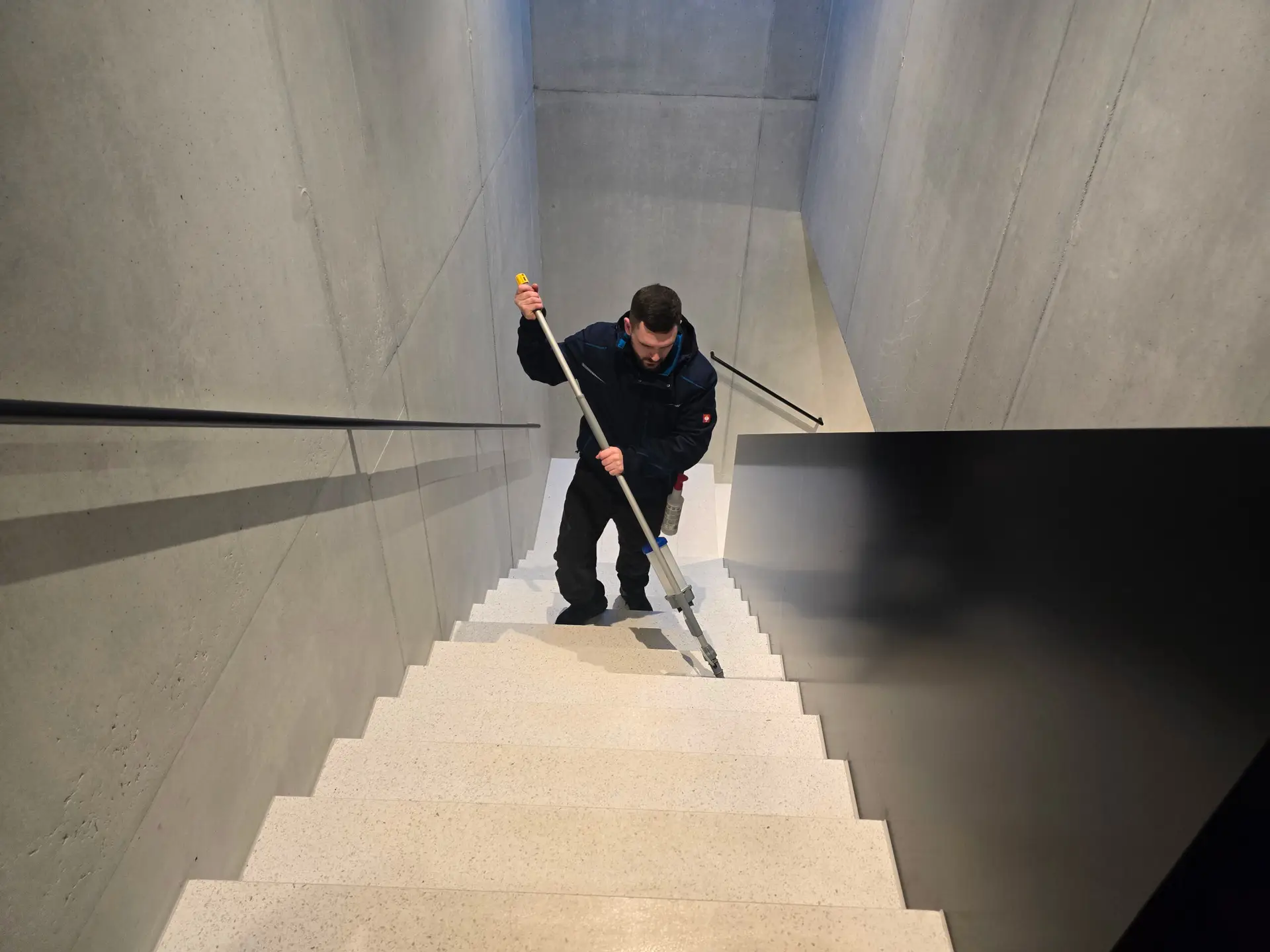 Reinigungskraft bei der Treppenhausreinigung in einem modernen Gebäude.